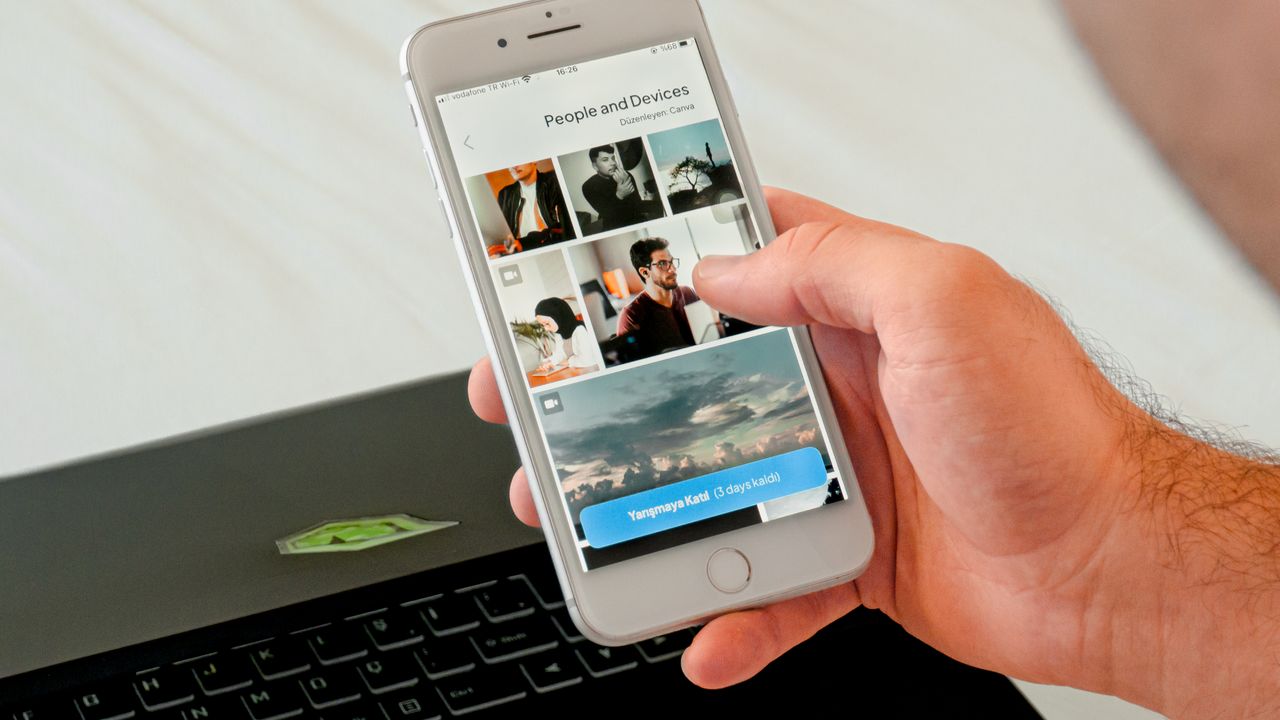 Home Close-up of a hand browsing photos on a smartphone with a laptop in the background, showcasing technology use.