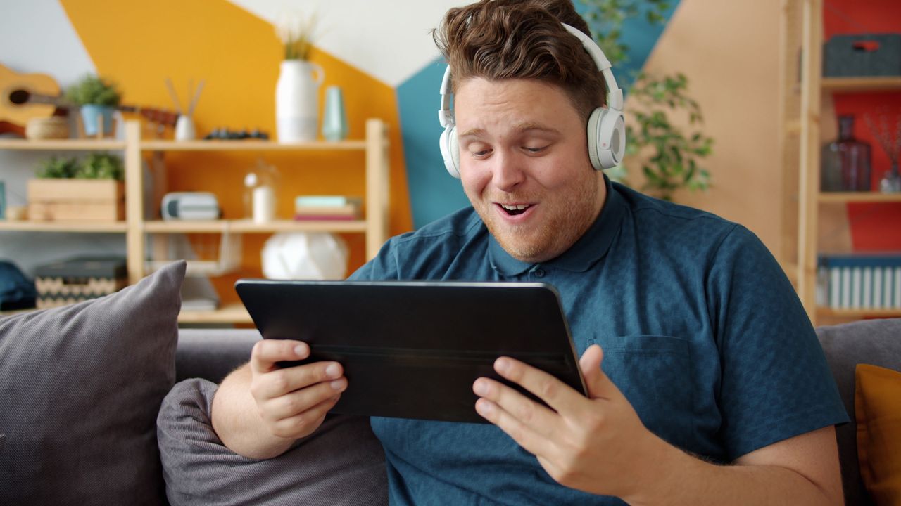 Home Smiling man with headphones using a tablet indoors, enjoying media content.