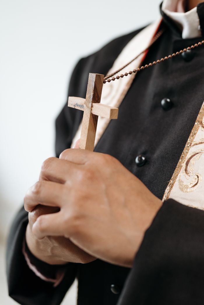 A religious leader holding a cross in prayer, symbolizing faith and devotion.