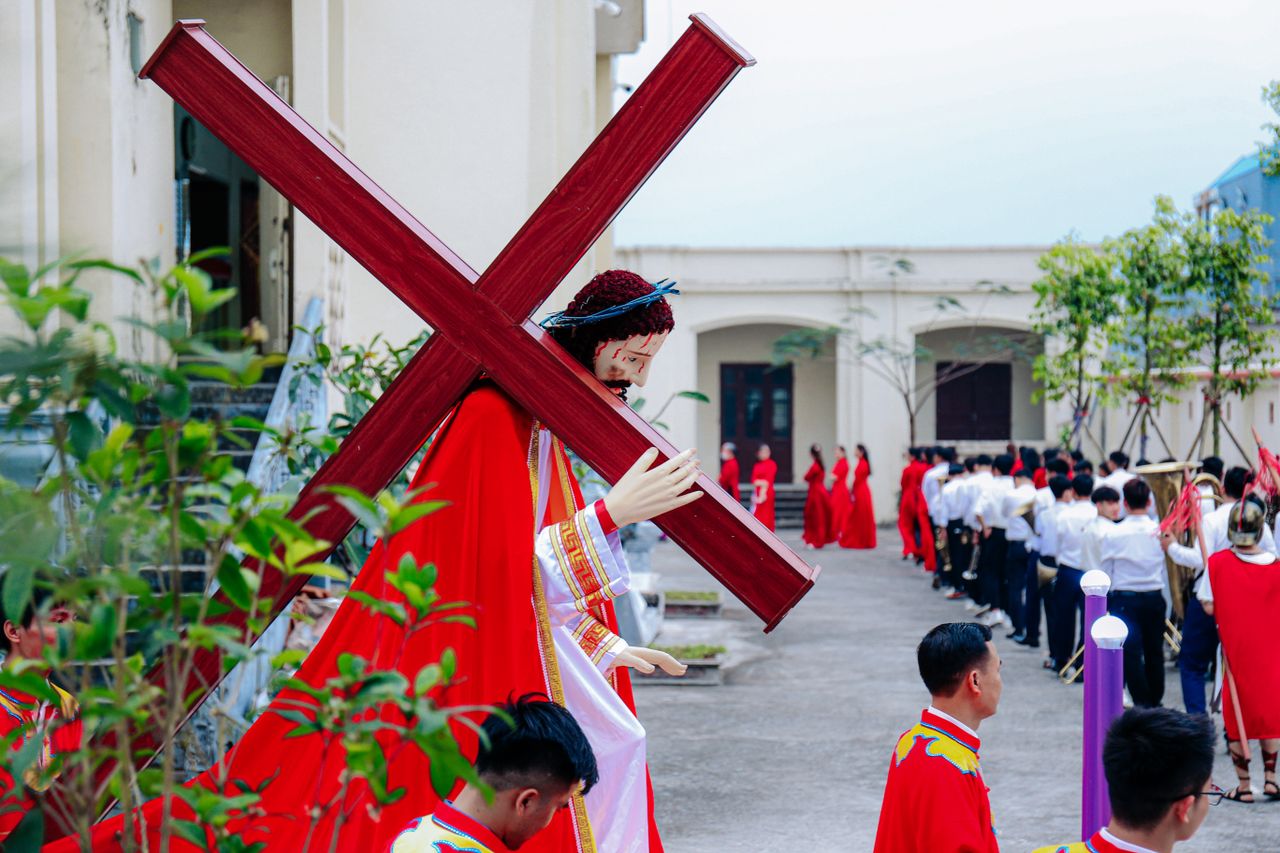 Emotional religious parade featuring a large cross and costumes, outdoors in Vietnam.