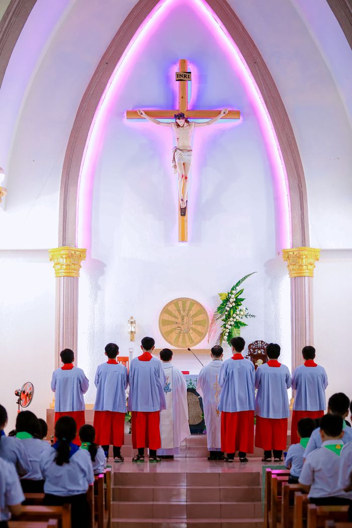 A religious ceremony inside a church with altar servers and a prominent crucifix.