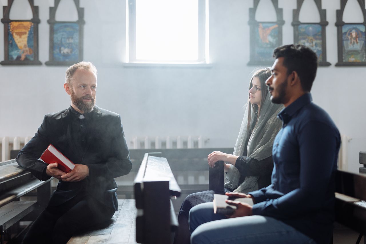 A priest converses with two people inside a church, highlighting religious dialogue and community.